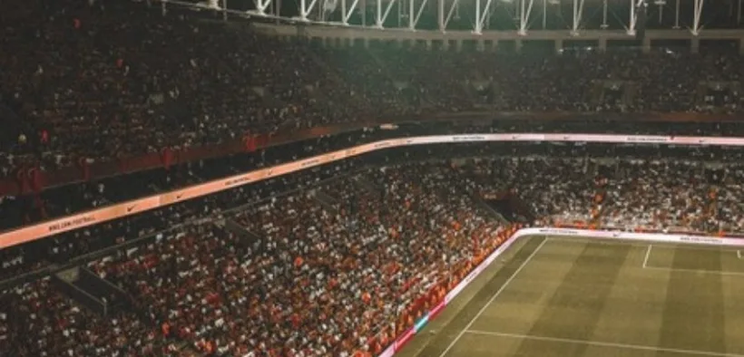 Estadio de futbol iluminado durante un partido nocturno con las gradas llenas