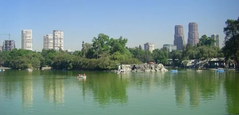 Lago de Chapultepec con lanchas, árboles y edificios al fondo en un día despejado