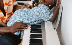 Bebé explora las teclas de un piano con acompañamiento de una persona adulta, imagen contextual