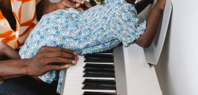 Bebé explora las teclas de un piano con acompañamiento de una persona adulta, imagen contextual