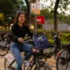 Mujer sonríe sobre una bicicleta compartida junto a una cicloestación al atardecer