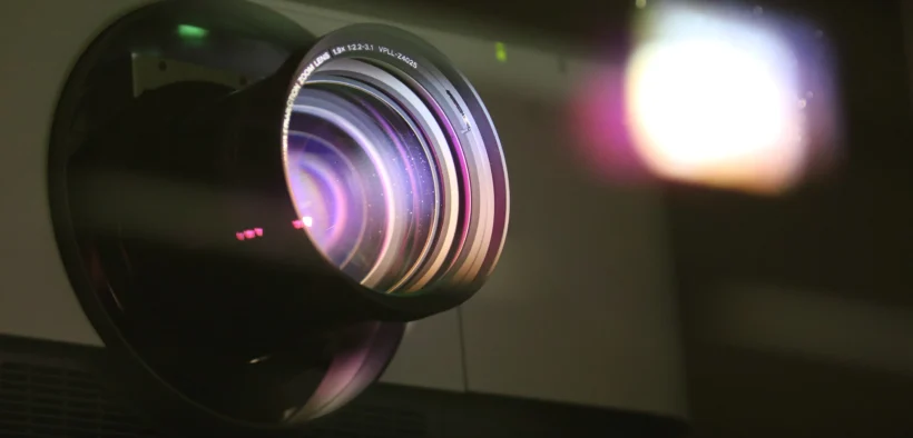 Detalle de la lente iluminada de un proyector; fotografía contextual de Ann H