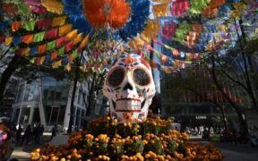Calavera monumental con papel picado y flores de cempasúchil en un camellón de la Ciudad de México