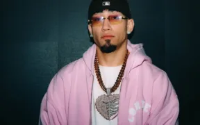 Retrato de Omar Courtz con sudadera rosa, lentes y cadenas