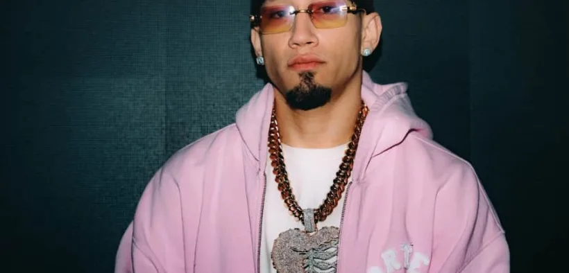 Retrato de Omar Courtz con sudadera rosa, lentes y cadenas