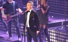 Robbie Williams canta durante un concierto con un micrófono en la mano