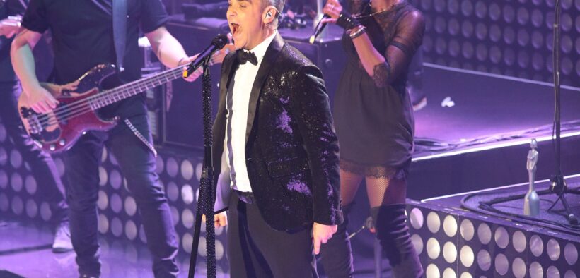Robbie Williams canta durante un concierto con un micrófono en la mano