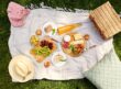 leisure and eating concept - close up of food, drinks and picnic basket on blanket on grass at summer park