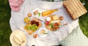 leisure and eating concept - close up of food, drinks and picnic basket on blanket on grass at summer park