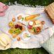 leisure and eating concept - close up of food, drinks and picnic basket on blanket on grass at summer park