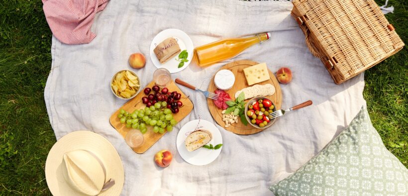 leisure and eating concept - close up of food, drinks and picnic basket on blanket on grass at summer park