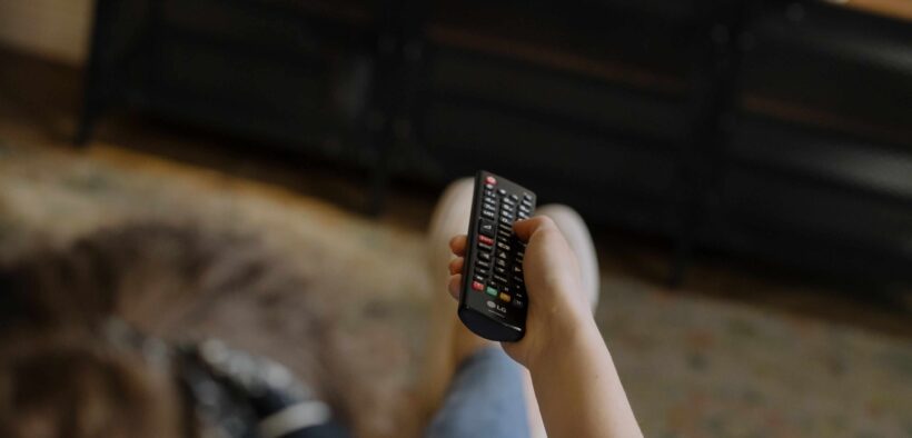 Persona sentada frente a un televisor sostiene un control remoto.